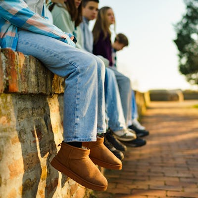 Close-up of a group of teenage friends hang their legs on a brick wall to relax