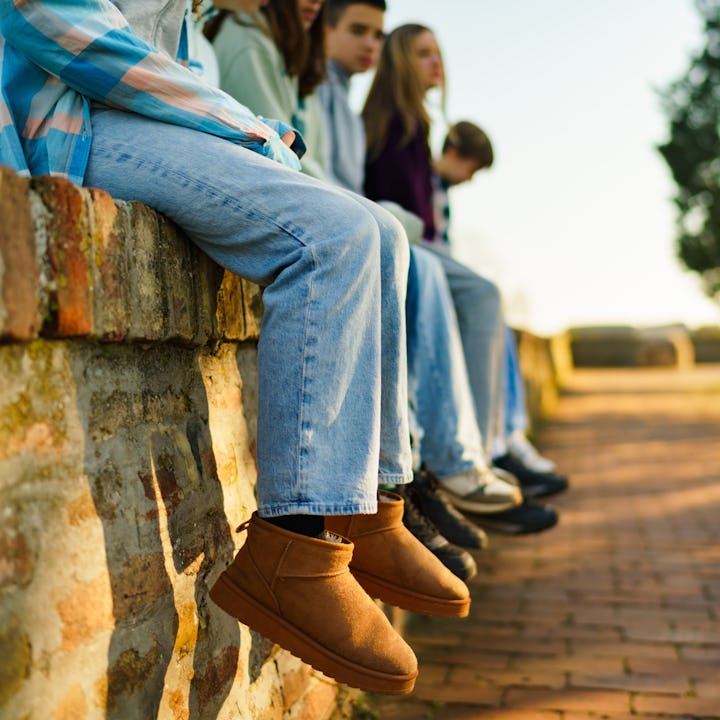 Close-up of a group of teenage friends hang their legs on a brick wall to relax