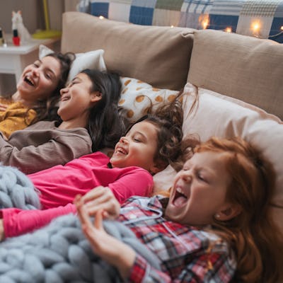 Portrait of four best friends during a sleepover party, lying in bed and laughing.