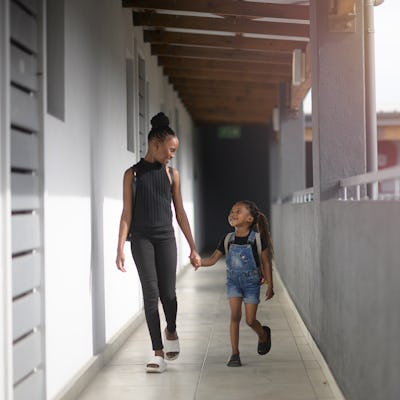 A teenager walks hand in hand with a younger sibling. The two smile at one another.