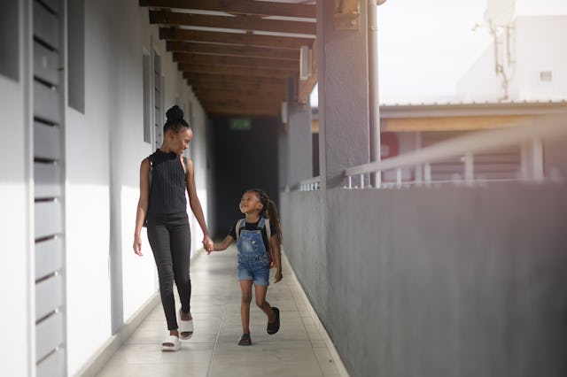 A teenager walks hand in hand with a younger sibling. The two smile at one another.