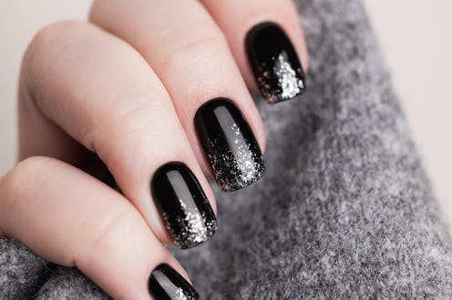 Female hand with beautiful manicure - black color gel nails with silver glitter, closeup fingers. Na...