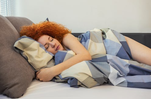 Portrait of a beautiful young woman with red curly hair sleeping in bed