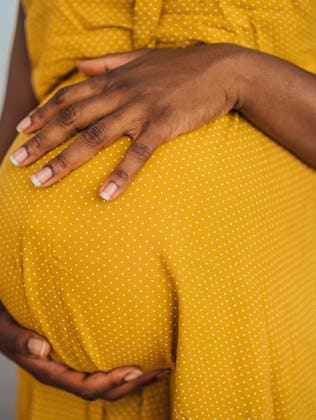 Close-up of pregnant woman in yellow dress embracing her pregnant belly.