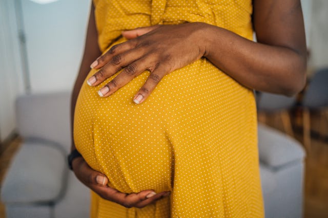 Close-up of pregnant woman in yellow dress embracing her pregnant belly.
