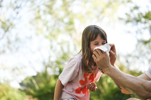 Preschool girl sneezing in park.