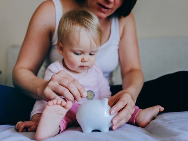 Mother and her baby girl putting coins into piggy bank.