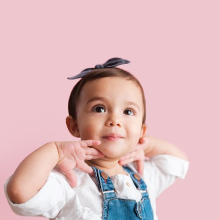 A close up photo of a little girl putting her hands on her neck as she looks up away from the camera...
