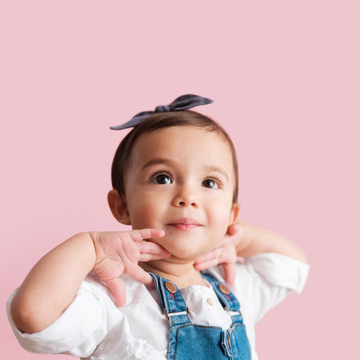 A close up photo of a little girl putting her hands on her neck as she looks up away from the camera...