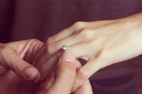 A close-up of a man placing a diamond engagement ring on a womans hand, symbolizing love and commitm...