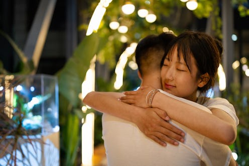 A tender embrace between a man and woman under soft lighting, set against a backdrop of greenery and...