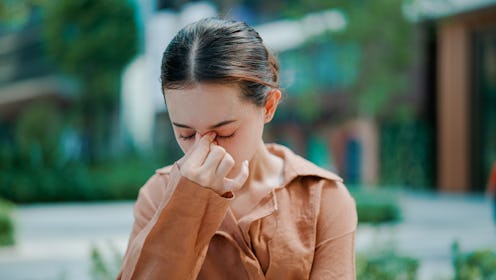 A young Asian female office worker pinching the bridge of her nose while feeling stressed from work.