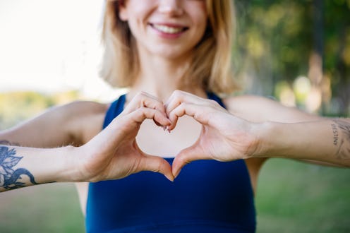 Fitness, happy and heart hands of young woman in nature after running for health