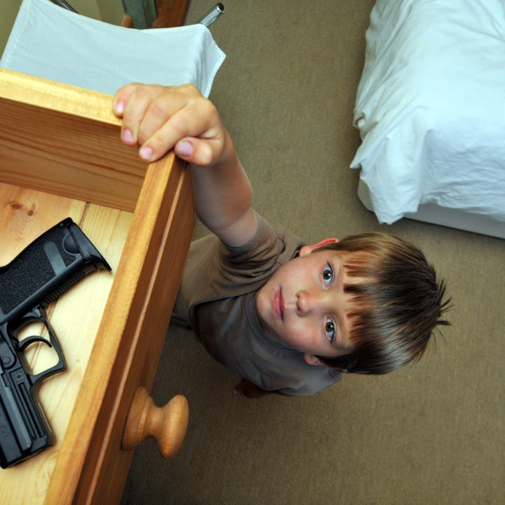 A young boy reaches for a drawer in a bedroom, with a handgun visible on the open drawer. The room h...