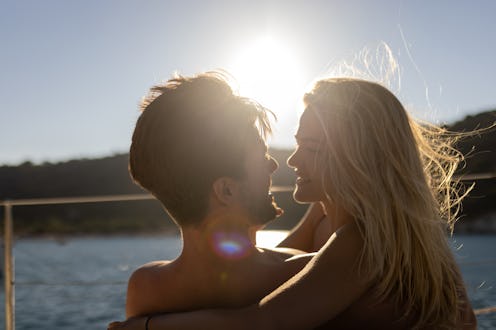 Beautiful young couple relaxing and enjoying together on sailboat cockpit at sunset. They are affect...