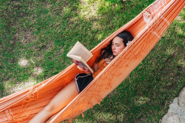 view on teenage girl reading book in hammock in the garden in summer