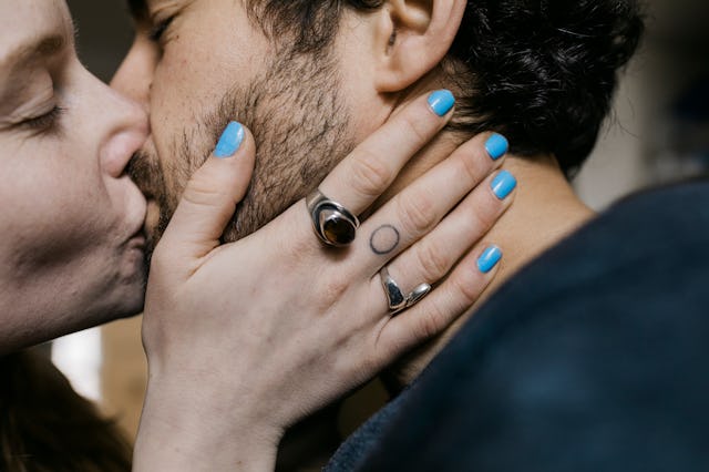 A woman with blue nail polish and a tattoo on her middle finger kissing her boyfriend she met online...