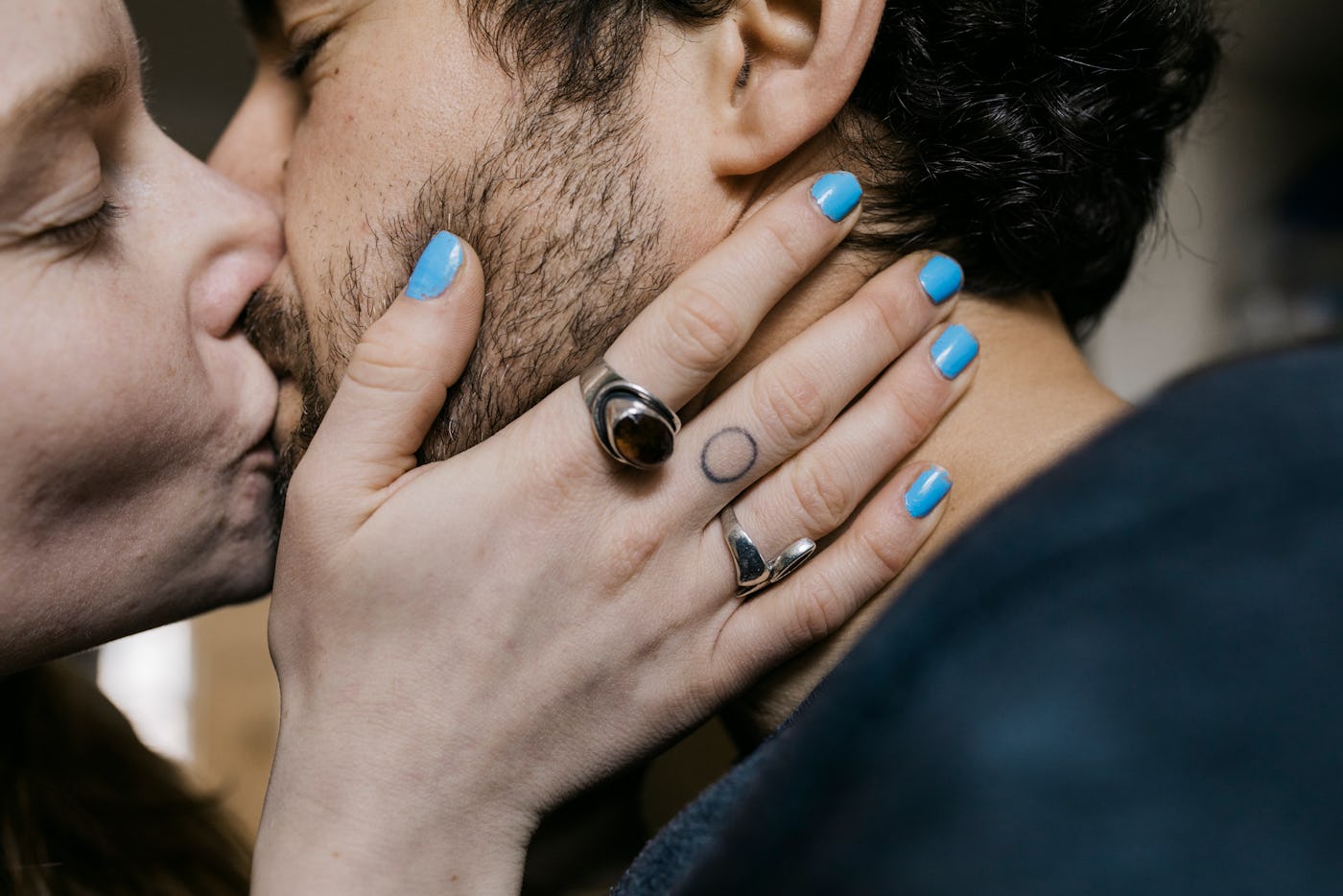 A woman with blue nail polish and a tattoo on her middle finger kissing her boyfriend she met online.