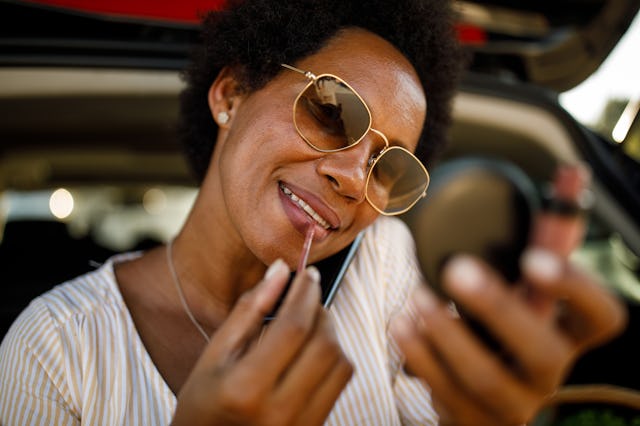 Headshot of joyful mid adult African American woman sitting in her car trunk, looking in the hand mi...