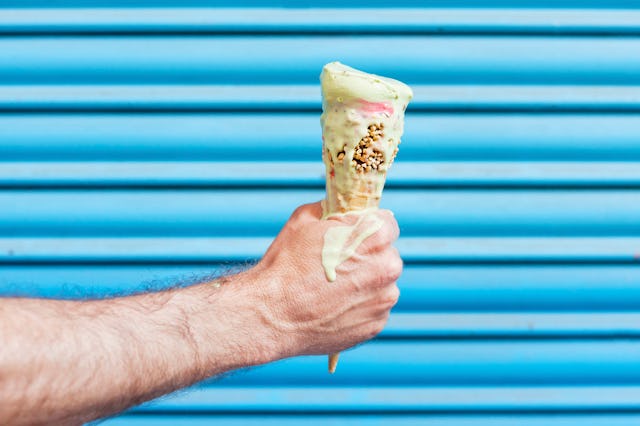 Caucasian adult male hand holding a melting ice cream cone in front of a vibrant blue shutter backgr...