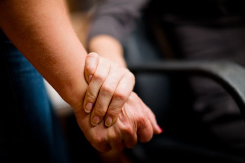 In a close-up shot, two unrecognisable women clasp hands in a gesture of support and affection. The ...