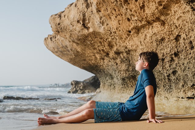Relaxed teenage boy at the sea during sunset with eyes closed. Rocky cliffs and waves are visible in...