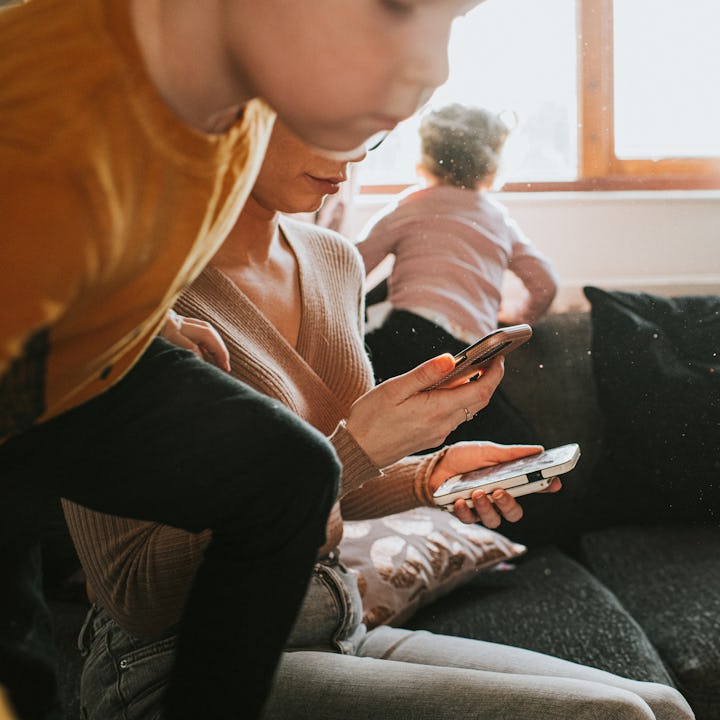 A single mum sits on a sofa looking down at two mobile phones. She attempts to stay focused and work...