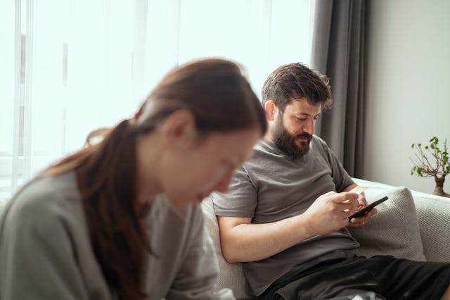 Man holding a smartphone and credit card to make an online purchase while his wife browses on a digi...