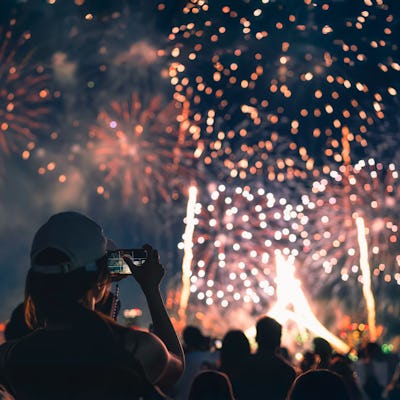 The back of a girl in a baseball cap filming a fireworks display on her mobile phone