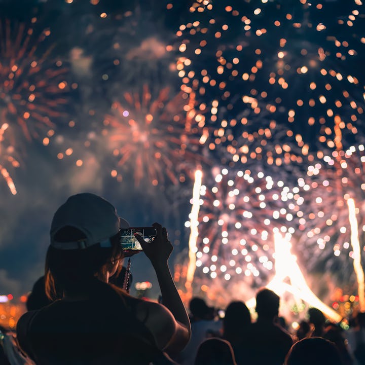 The back of a girl in a baseball cap filming a fireworks display on her mobile phone