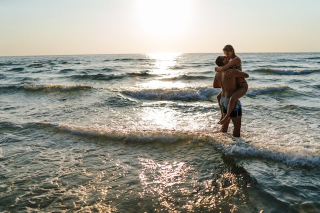 Handsome young man carrying and kissing his girlfriend in sea shallow at sunset
