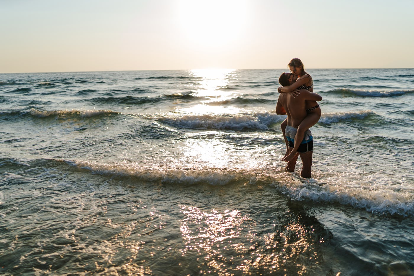 Handsome young man carrying and kissing his girlfriend in sea shallow at sunset