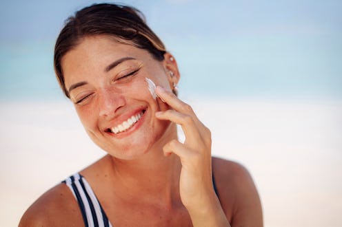 A cheerful woman with light brown hair and freckles applies sunscreen on a sunny day at a tropical M...