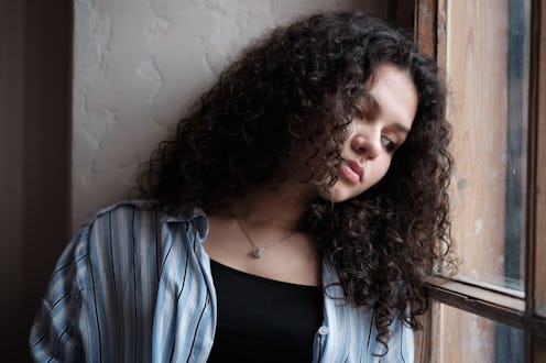 Gen Z Loneliness. Sad young girl standing by window feeling lonely. Depressed teenage girl looking o...
