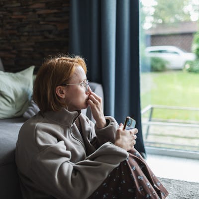 Mid adult woman sitting with mobile at home, sad and depressed