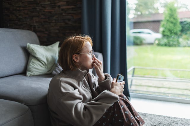 Mid adult woman sitting with mobile at home, sad and depressed