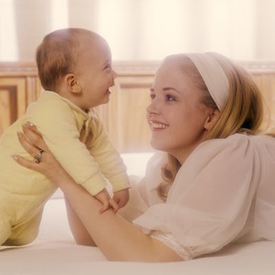 1970s WOMAN MOTHER IN WHITE HOLDING BABY IN YELLOW (Photo by Photo Media/ClassicStock/Getty Images)