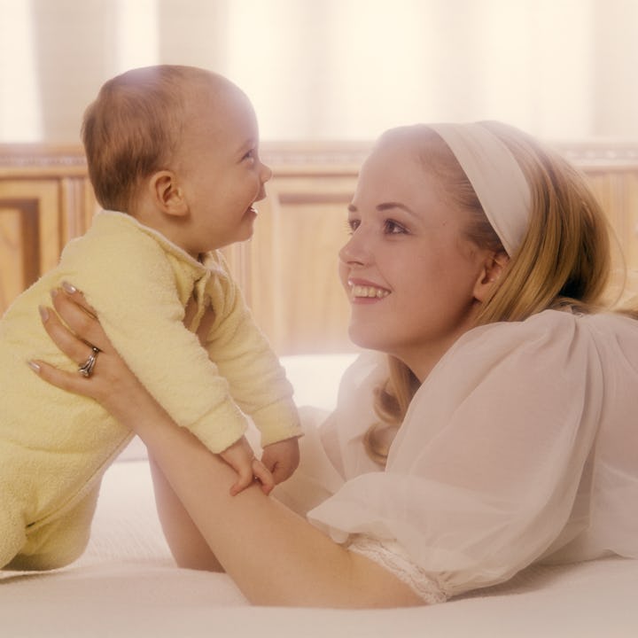 1970s WOMAN MOTHER IN WHITE HOLDING BABY IN YELLOW  (Photo by Photo Media/ClassicStock/Getty Images)