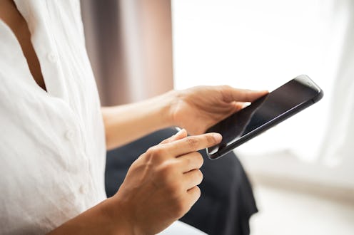 A person dressed casually interacts with a smartphone in a well-lit room, focusing on the screen.