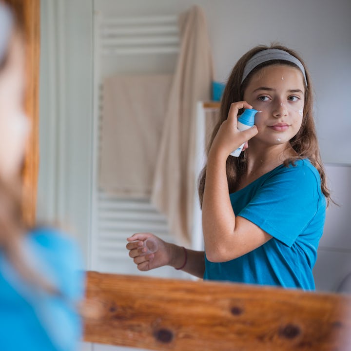Adolescent girl applying face cream onto her face in a bathroom