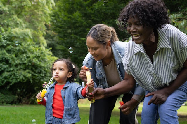 Three generations of women: grandmother, mother, and daughter, blowing bubbles in the park.