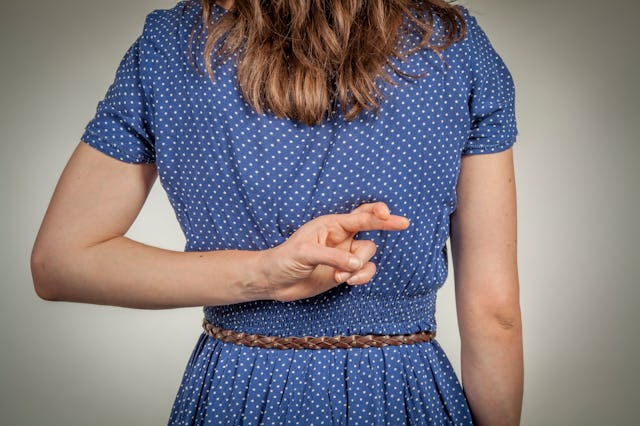 A woman stands with her back to the camera, wearing a blue polka dot dress. Her right hand is crossi...