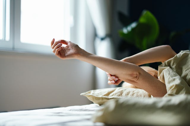 Unrecognizable woman laying in bed in the morning. She is stretching her arms above her.