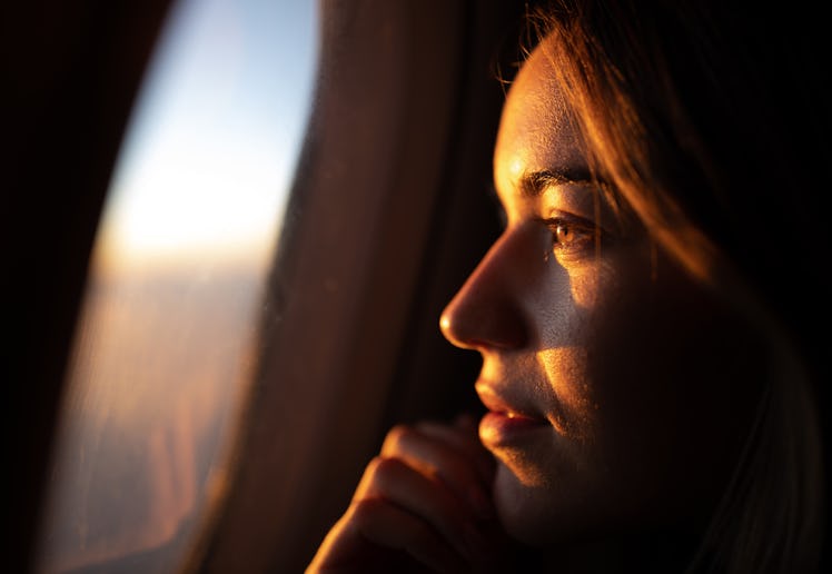 Close up of young woman day dreaming while looking through an airplane window at sunset.
