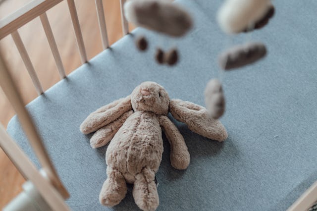 Stylish Scandinavian newborn baby nursery with natural wooden baby cot, stuffed bunny and handmade h...