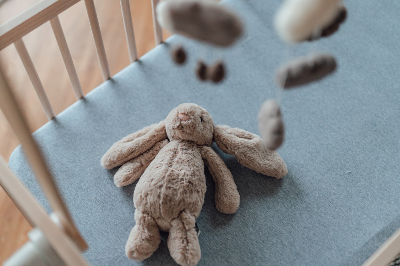 Stylish Scandinavian newborn baby nursery with natural wooden baby cot, stuffed bunny and handmade hanging mobile. Modern interior with white coloured walls and wooden flooring in the morning daylight. Getting ready for a new born! Welcome new born baby concept.