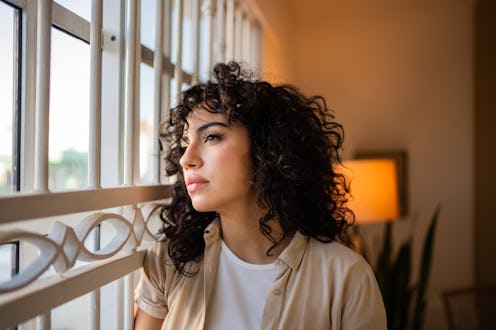 Young woman contemplating and looking through the window at home