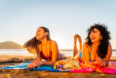 Young friends women talking lying on floor on the beach