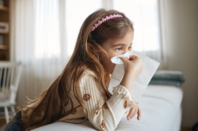 Sick girl blowing her nose with a tissue.