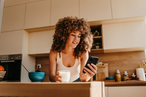 Young woman enjoying breakfast and checking her phone in a modern kitchen